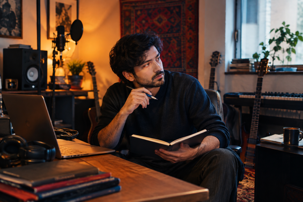 Musician in a cozy recording room, writing notes with a laptop.